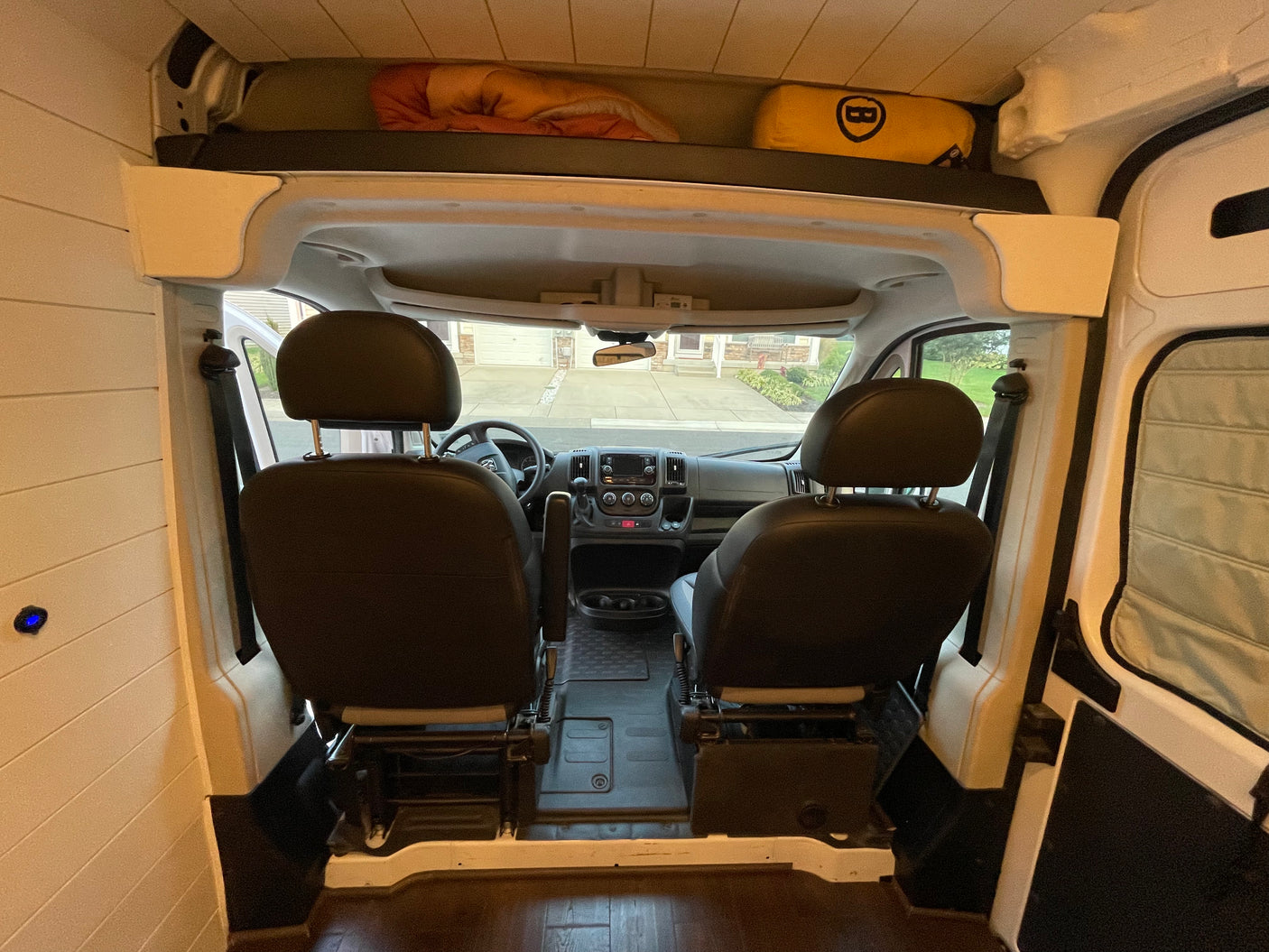 Inside an RV rental campervan, showing the front cab, driver/passenger seats, and overhead bed/storage area.