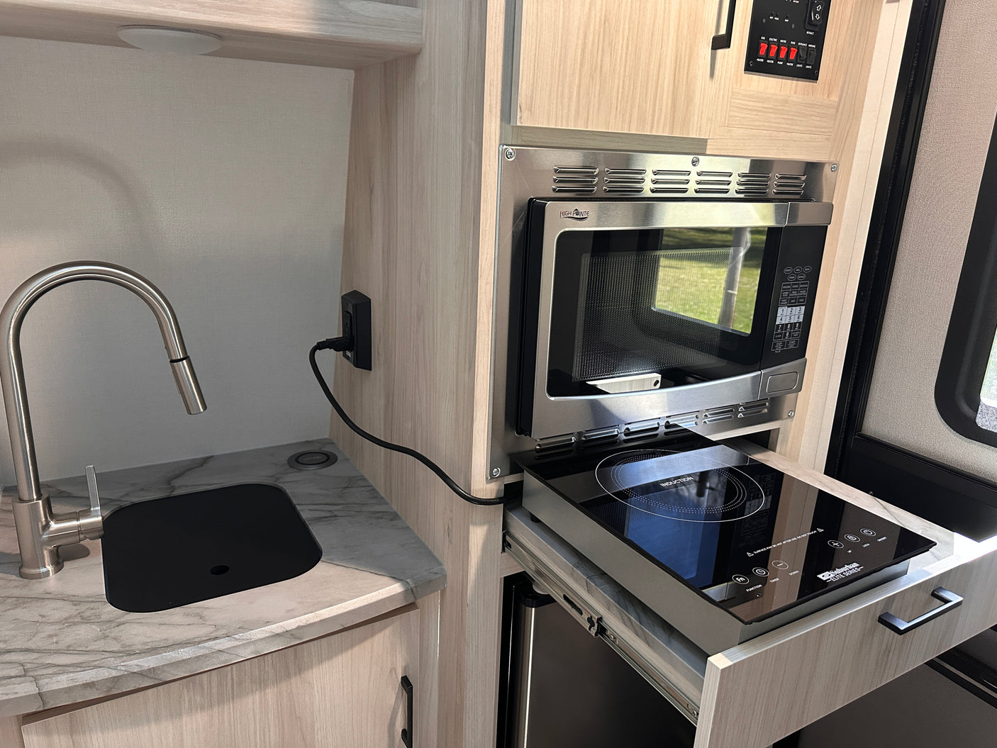This RV rental kitchenette features a modern sink, mounted microwave, and a space-saving pull-out induction cooktop.