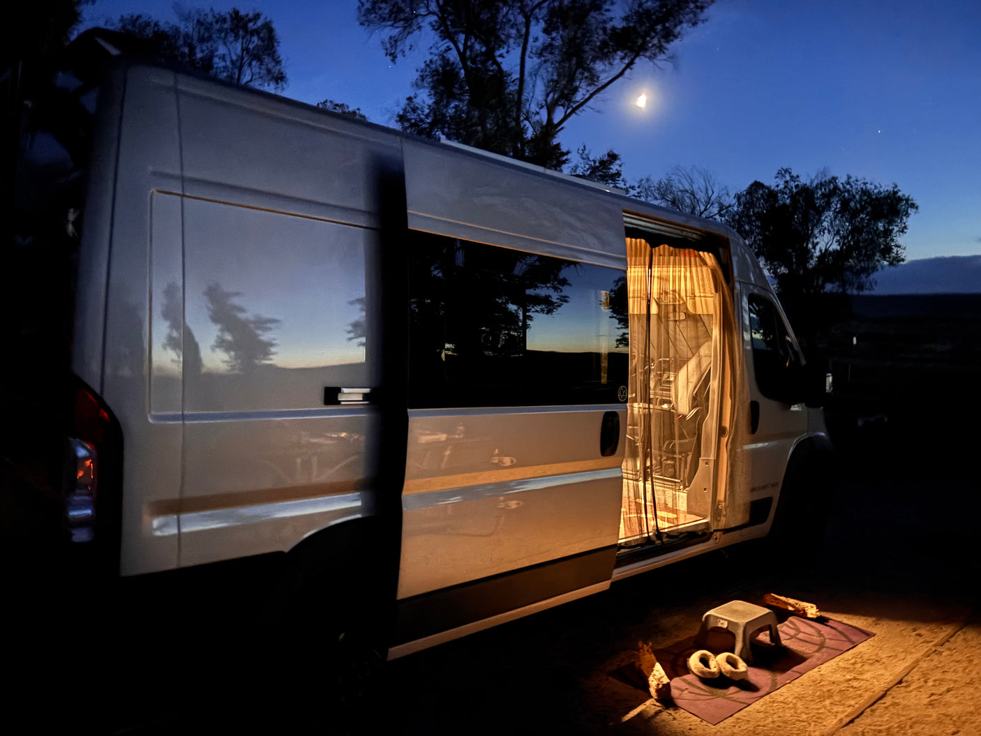 A cozy **rv rental** camper van, illuminated inside with an open door, rests under a serene crescent moon at night, perfect for **camping** adventures.