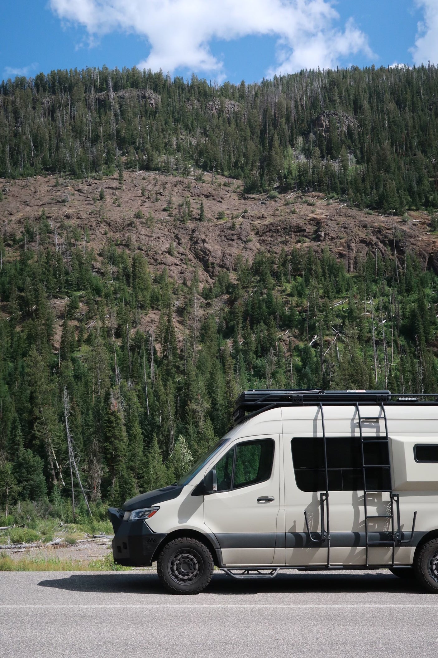 An RV rental camper van parked on a road with a dense, tree-covered mountain backdrop, perfect for outdoor adventure.