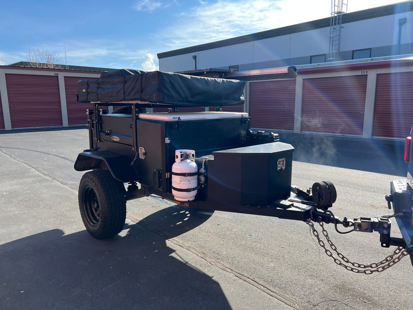 Dark overland trailer with rooftop tent & propane tank, ideal for your next RV rental adventure.
