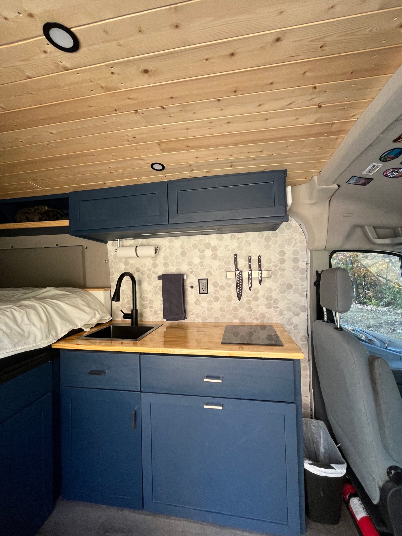 RV rental: Sleek camper van interior with wood ceiling, compact kitchen, black sink, induction cooktop, navy cabinets.