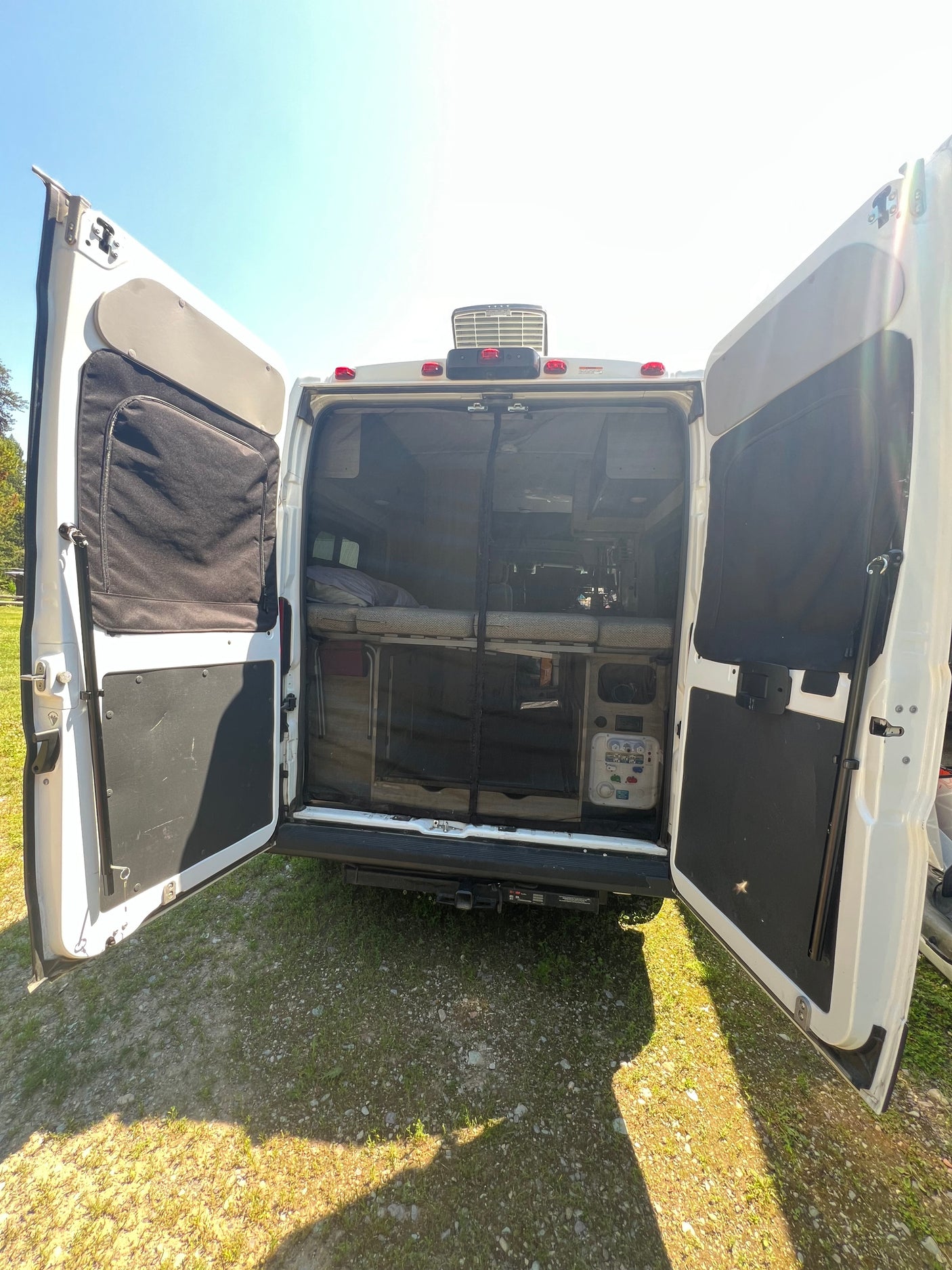 Back view of an RV rental camper van with open doors, revealing a cozy bed, storage, and bug screen. Ideal for van life adventures.