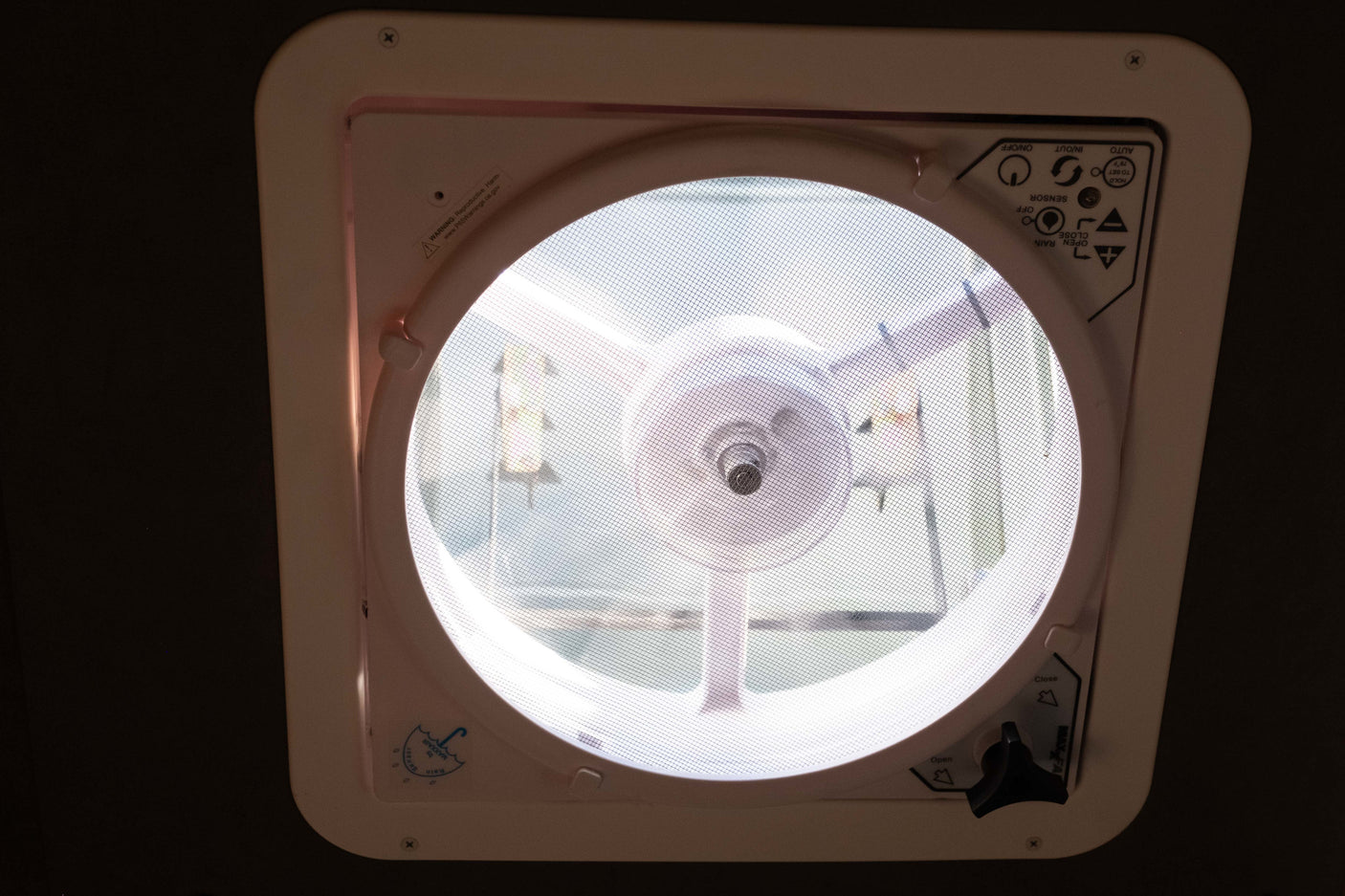 Inside an RV rental: a Maxxair ceiling fan and vent with controls, screen, and warning label, providing air flow.