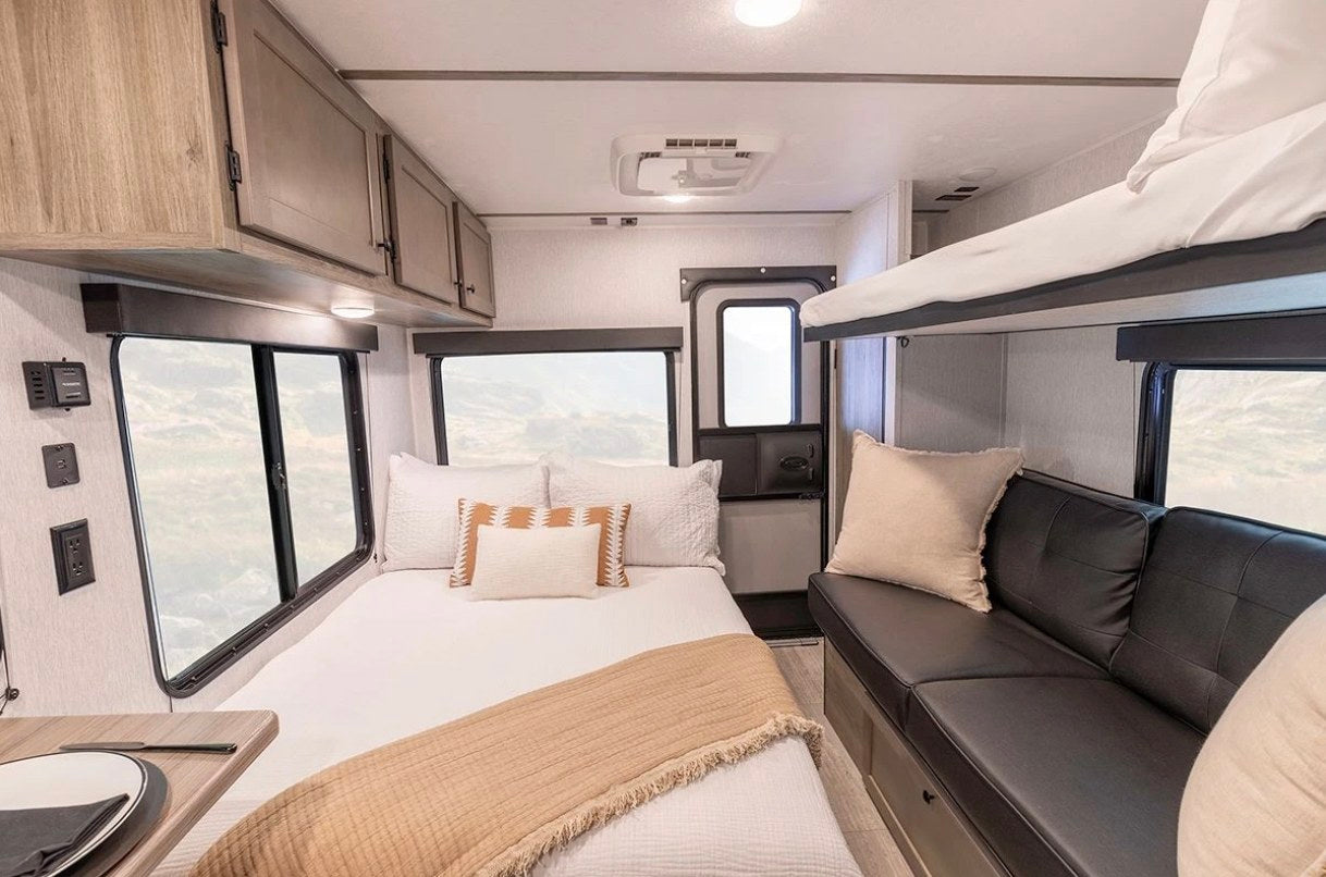 RV rental interior features a cozy bedroom with bunk beds, a comfy couch, and large windows. Ready for adventure!