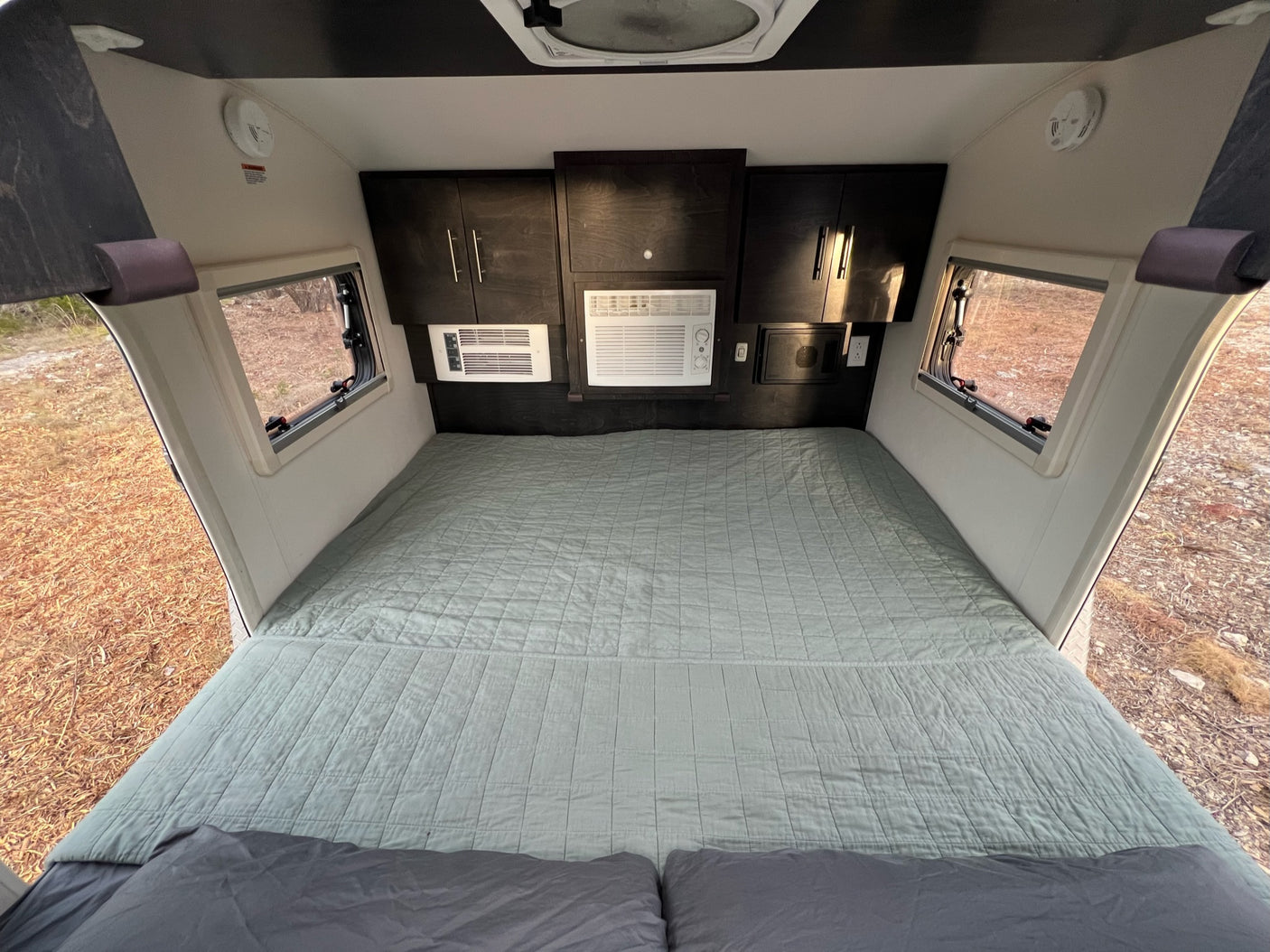 Cozy RV rental bedroom with large bed, wall AC unit, storage, and scenic window views. Perfect for travel.