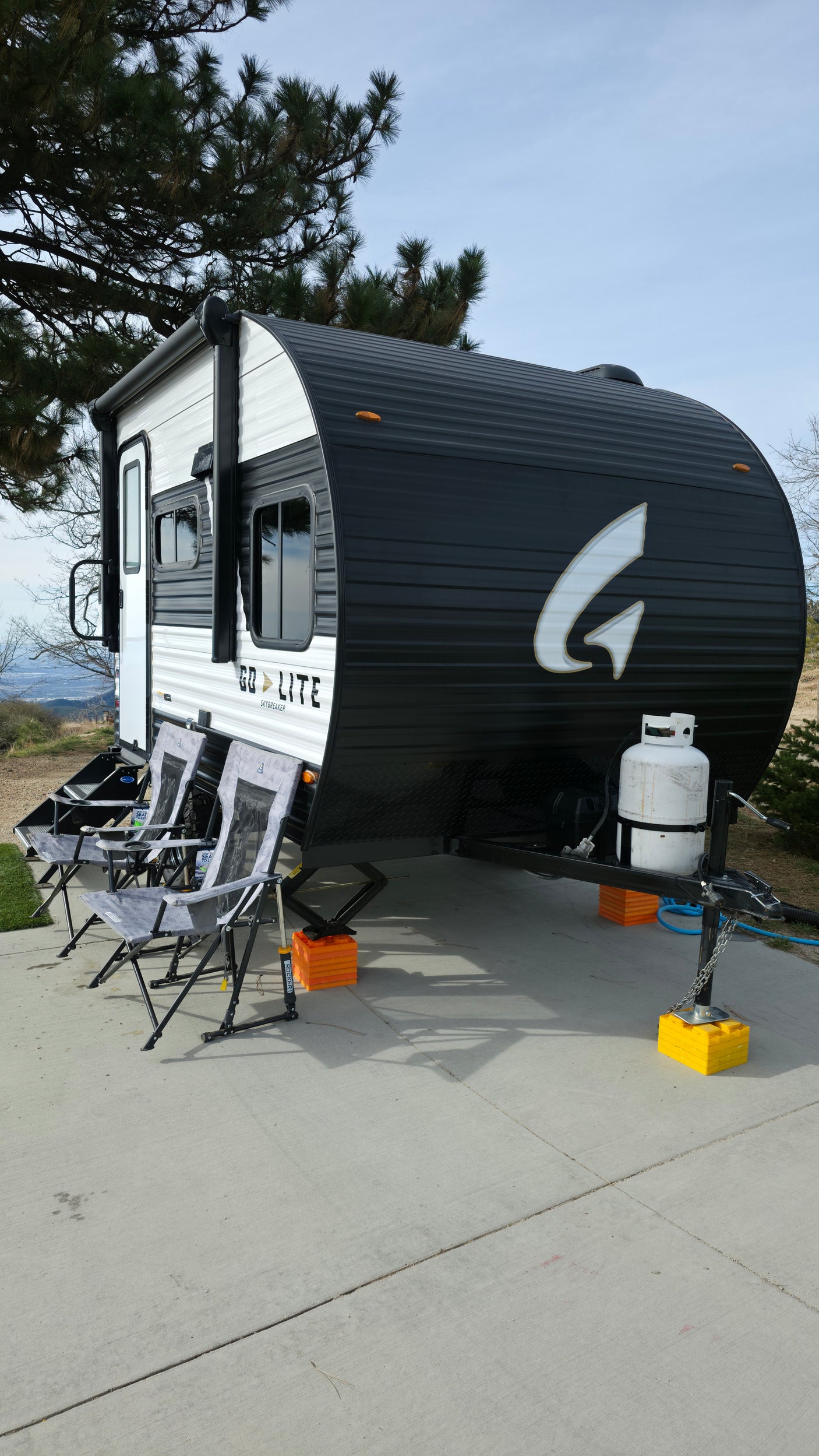 An rv rental, a sleek black and white travel trailer, parked outdoors with chairs, propane, and stabilizers for a comfortable stay.