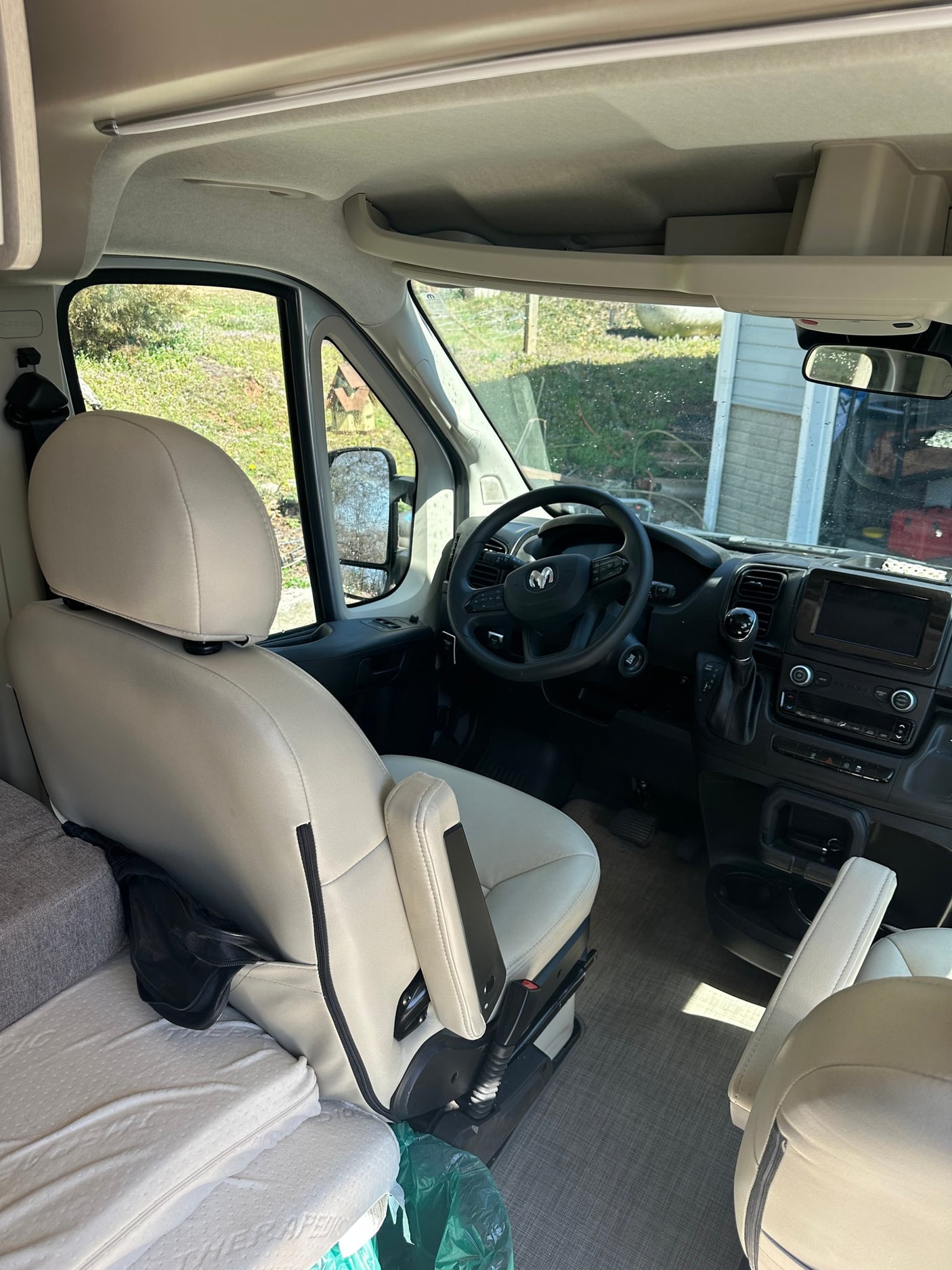 Inside a modern **rv rental**: view of the bright driver's cabin, dashboard, steering wheel, and front seats with an adjacent bed.