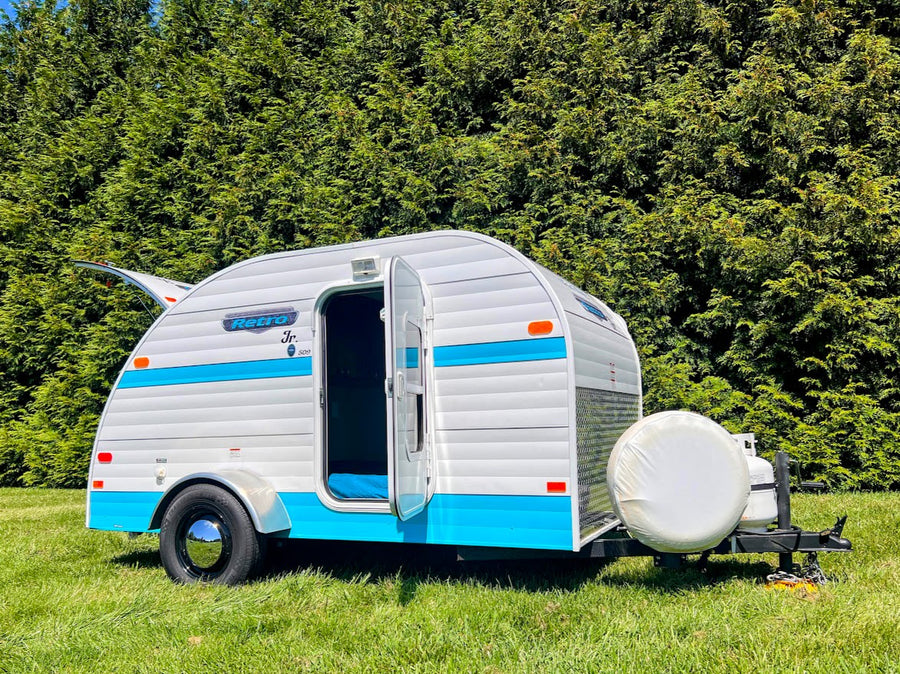 A charming white & blue Retro Jr. compact teardrop travel trailer for rv rental sits on grass