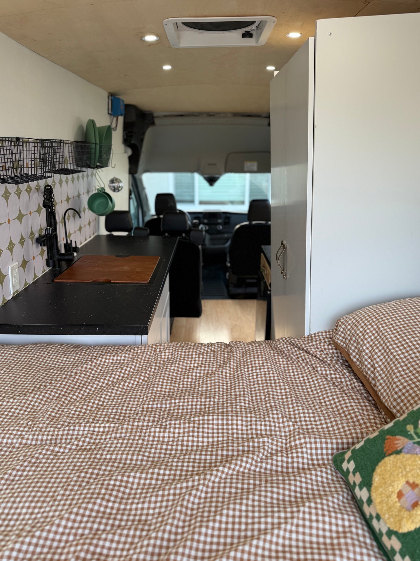 Cozy RV rental interior featuring a gingham bed, modern kitchen with a sink & backsplash, and a view into the front cabin.