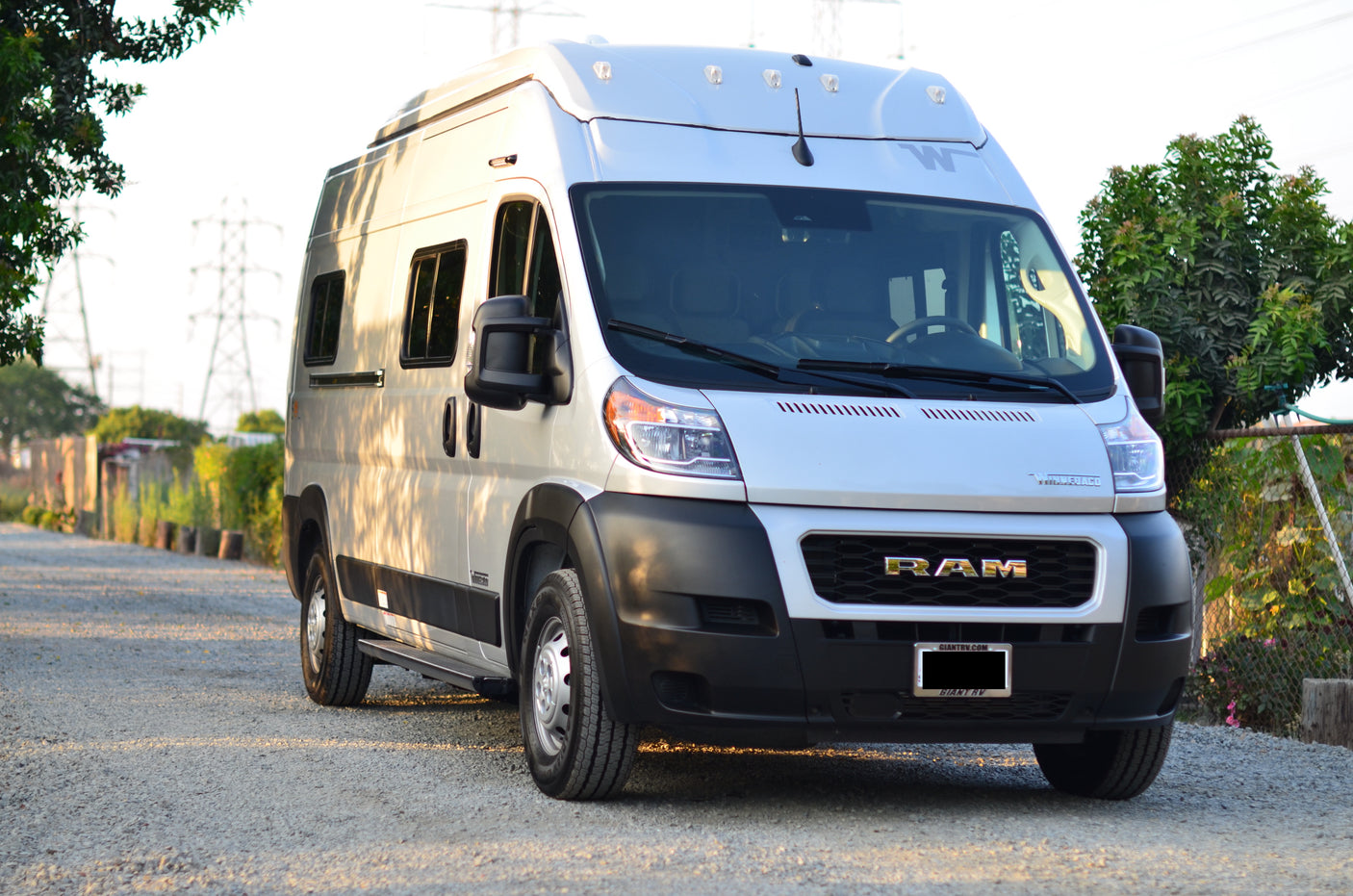 A white Winnebago Ram ProMaster camper van, perfect for your next rv rental adventure, parked on a gravel path.