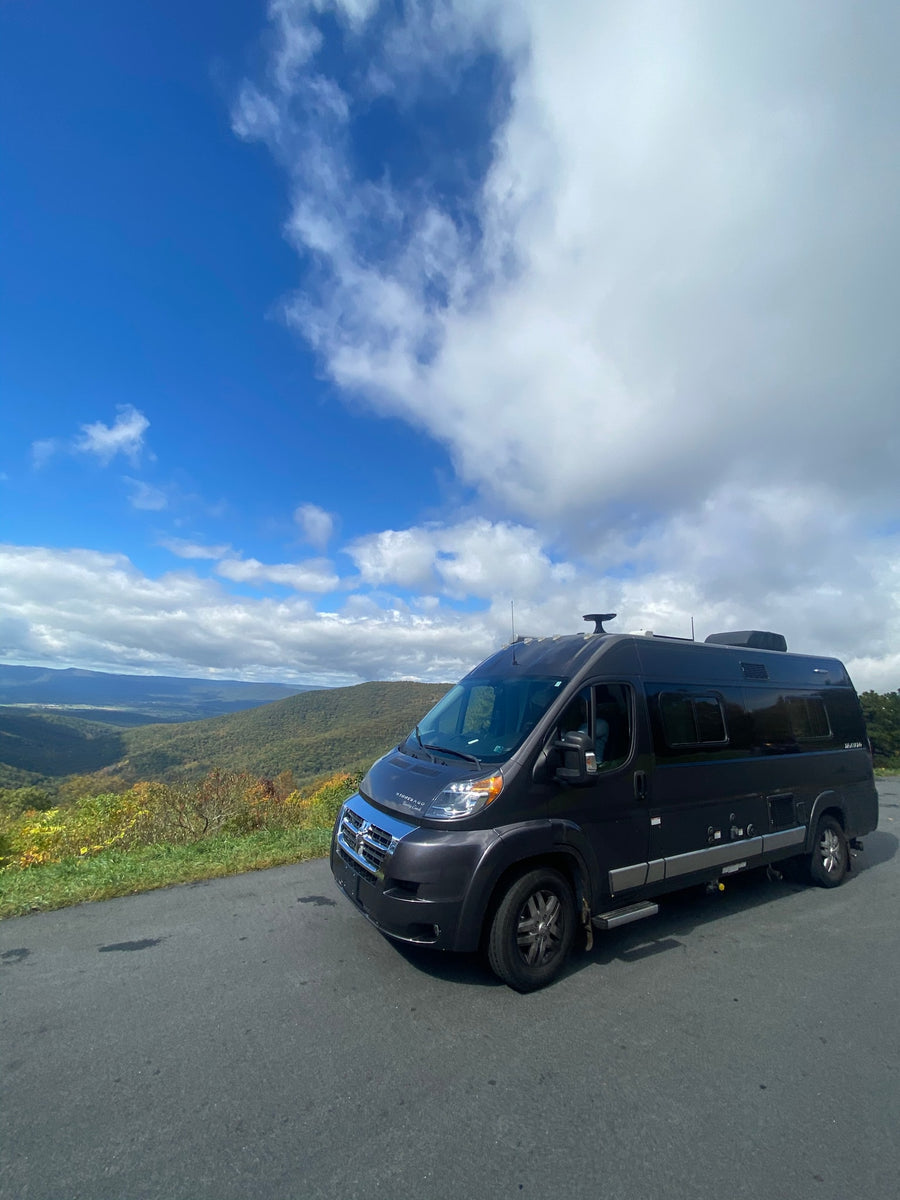 showcasing a vast landscape under cloudy skies.|Dark grey Winnebago RV rental parked on a mountain road