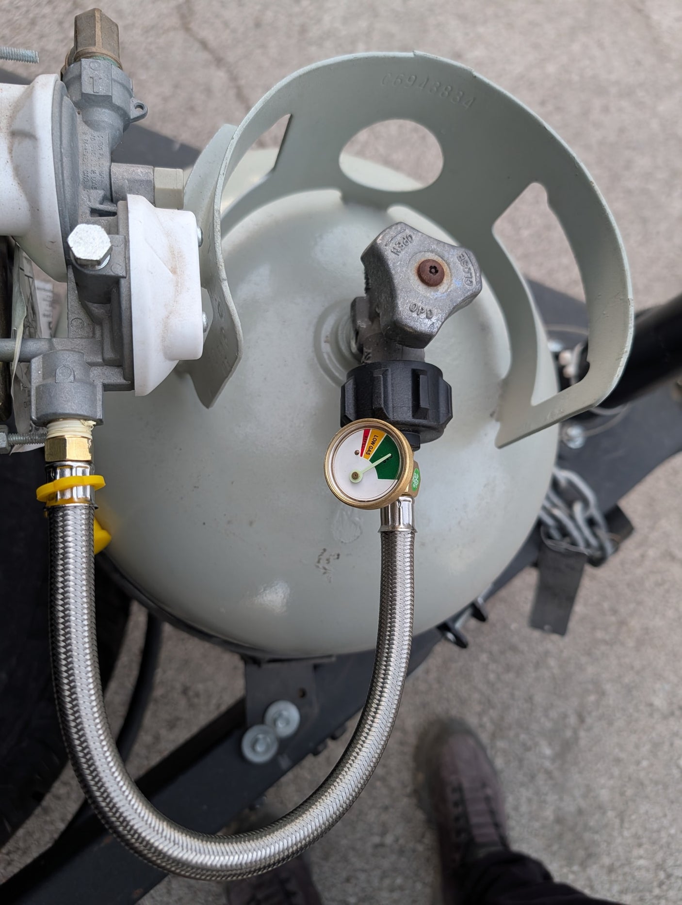 RV rental: Propane tank, gas gauge showing near full, connected to a regulator and braided hose.
