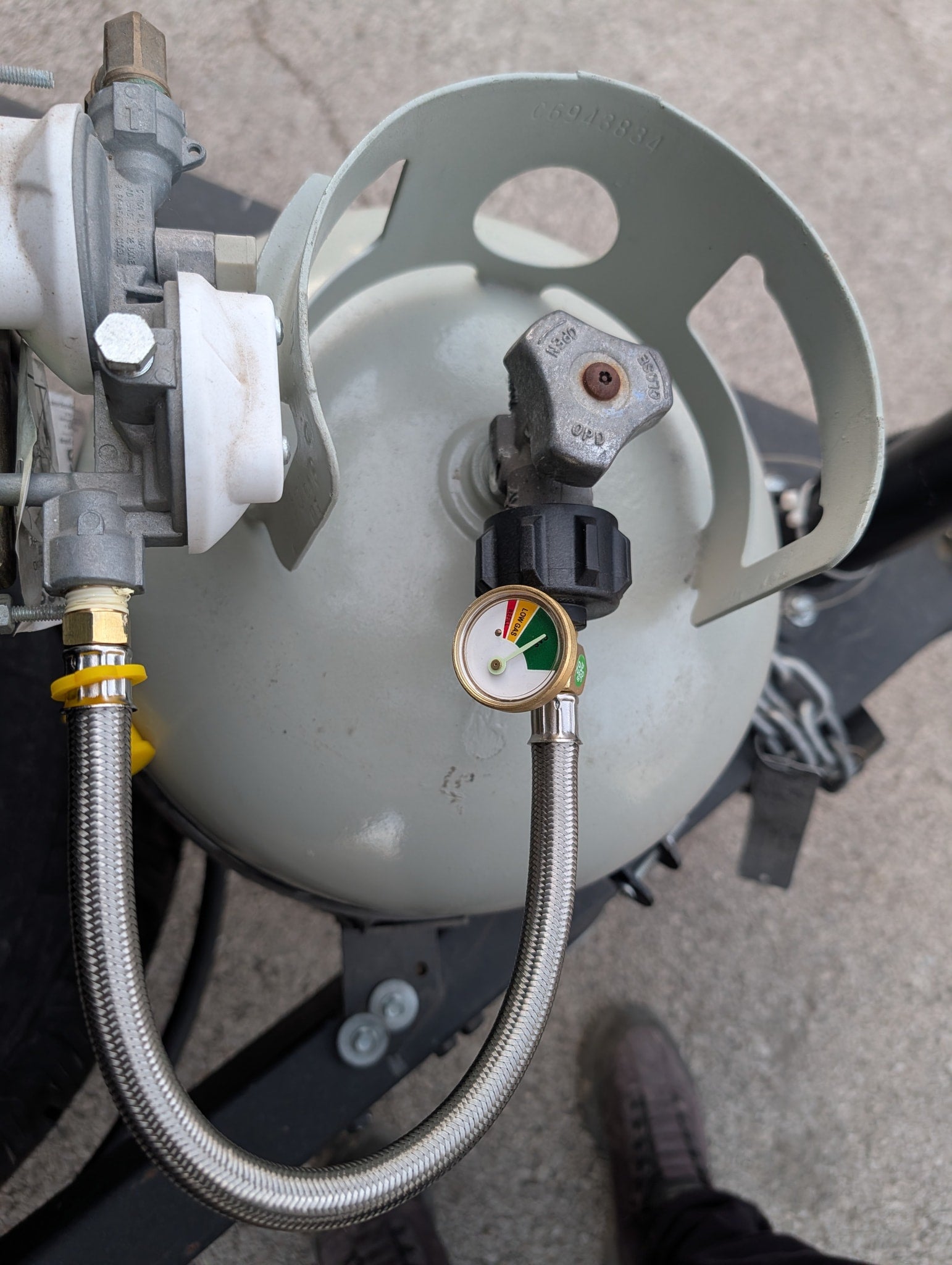 RV rental: Propane tank, gas gauge showing near full, connected to a regulator and braided hose.