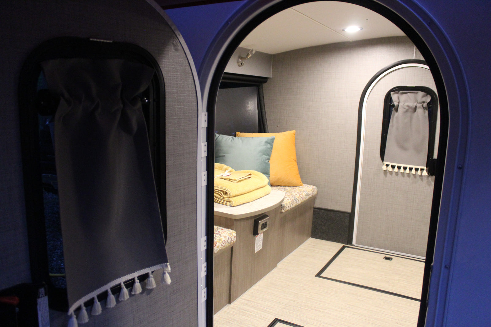Inside a modern RV rental, a compact living space is visible through arched doorways, featuring a bench, table, and soft furnishings.