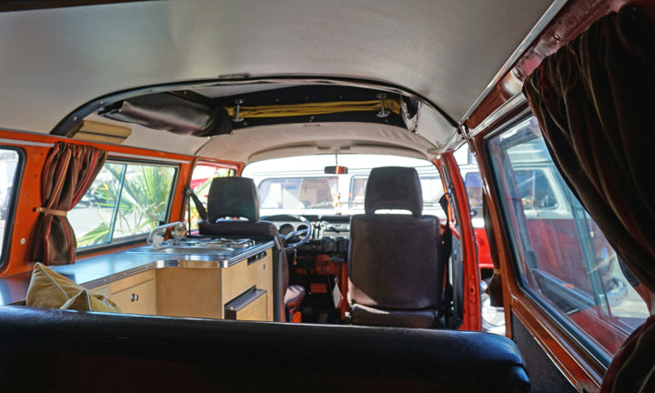 Inside a classic orange camper van, featuring a compact kitchen, front seats, and curtains. Ideal RV rental for trips.
