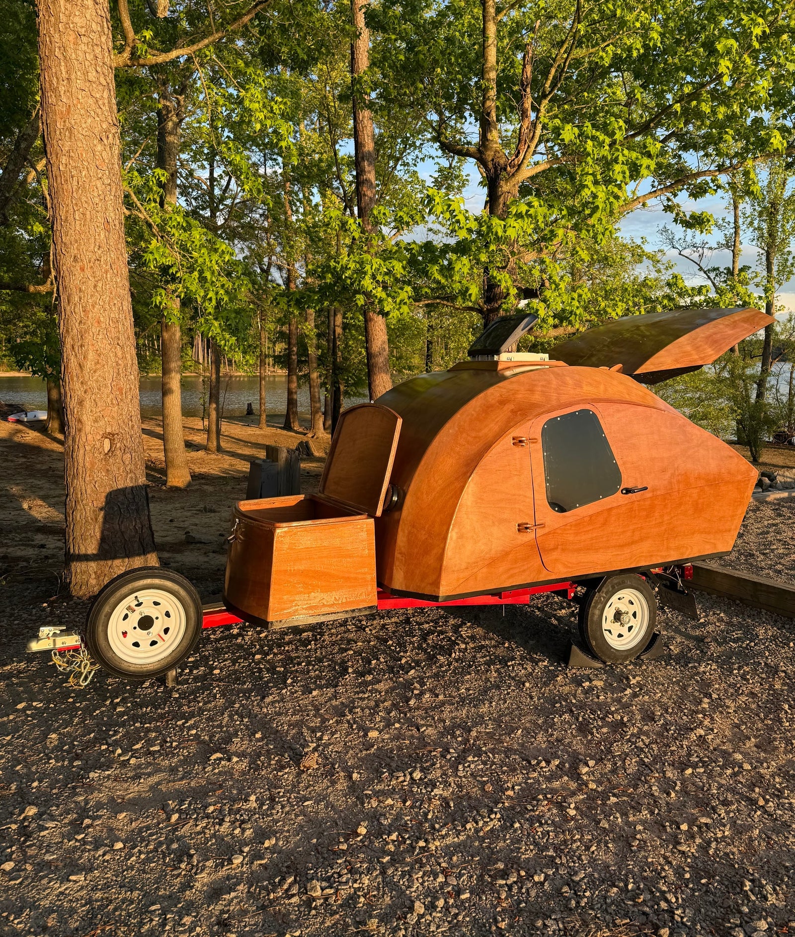A custom wooden teardrop camper parked by a lake; a charming