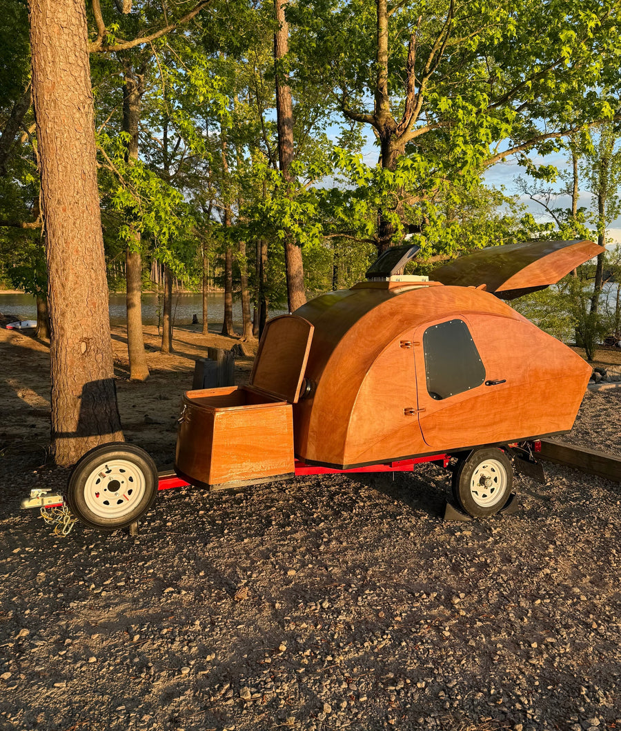 A custom wooden teardrop camper parked by a lake; a charming