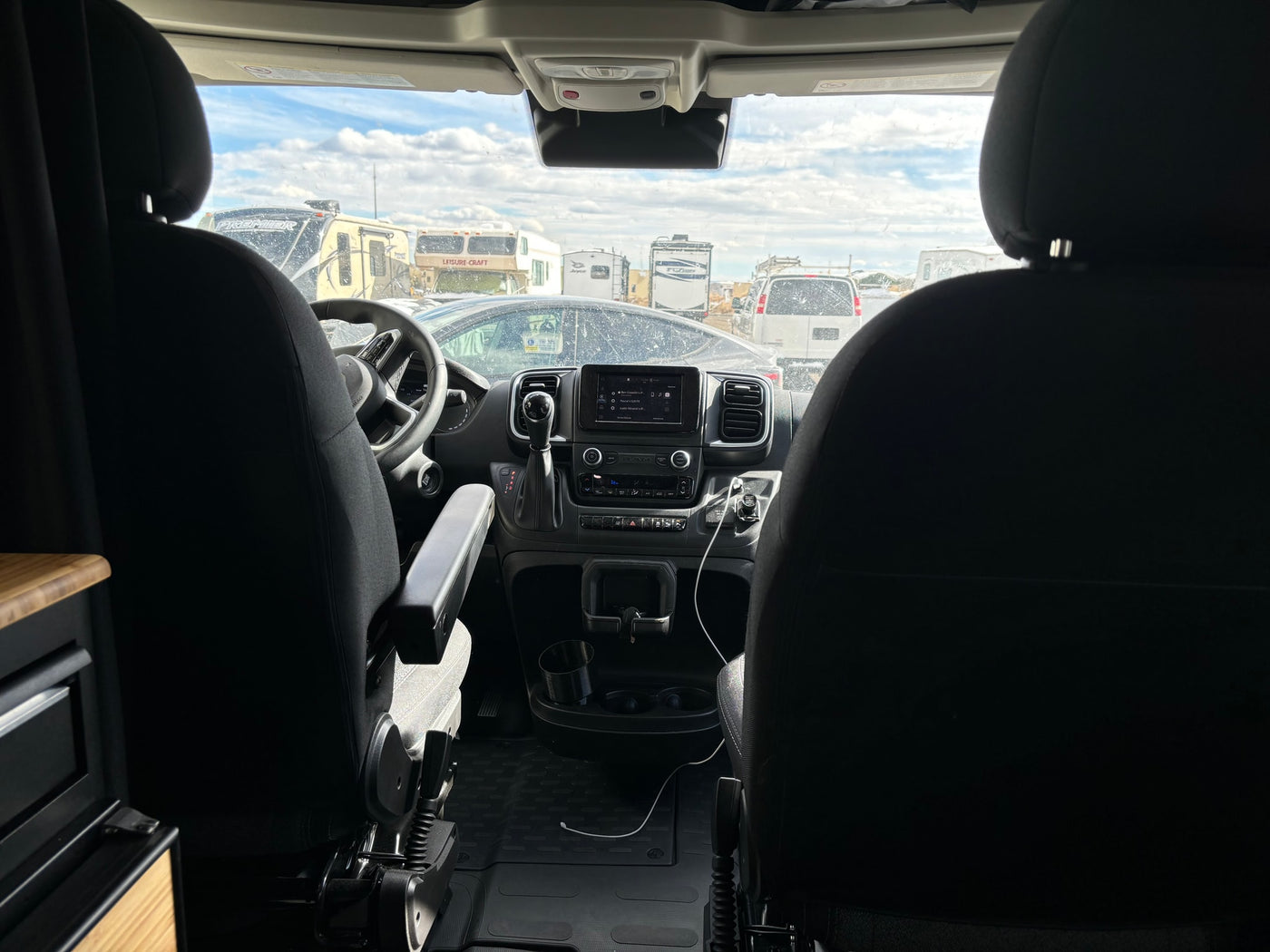 Front interior of an rv rental camper van, showing the dashboard and a view of multiple parked RVs through the windshield. — photo 10