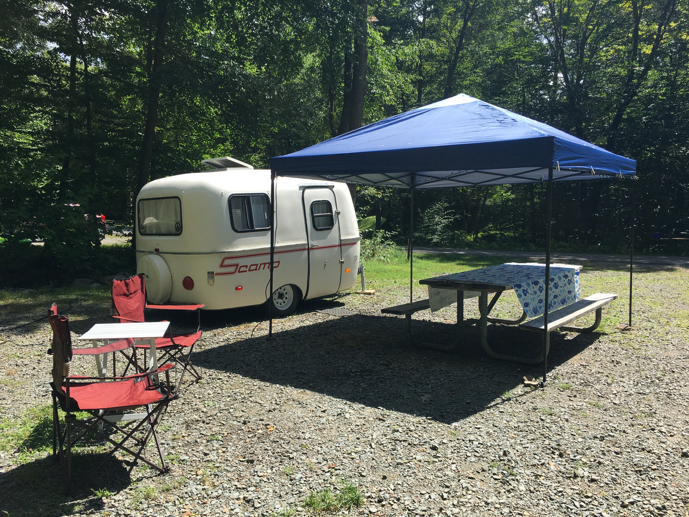 RV rental: Scamp trailer set up at a shaded campsite with a picnic area and chairs. — photo 3