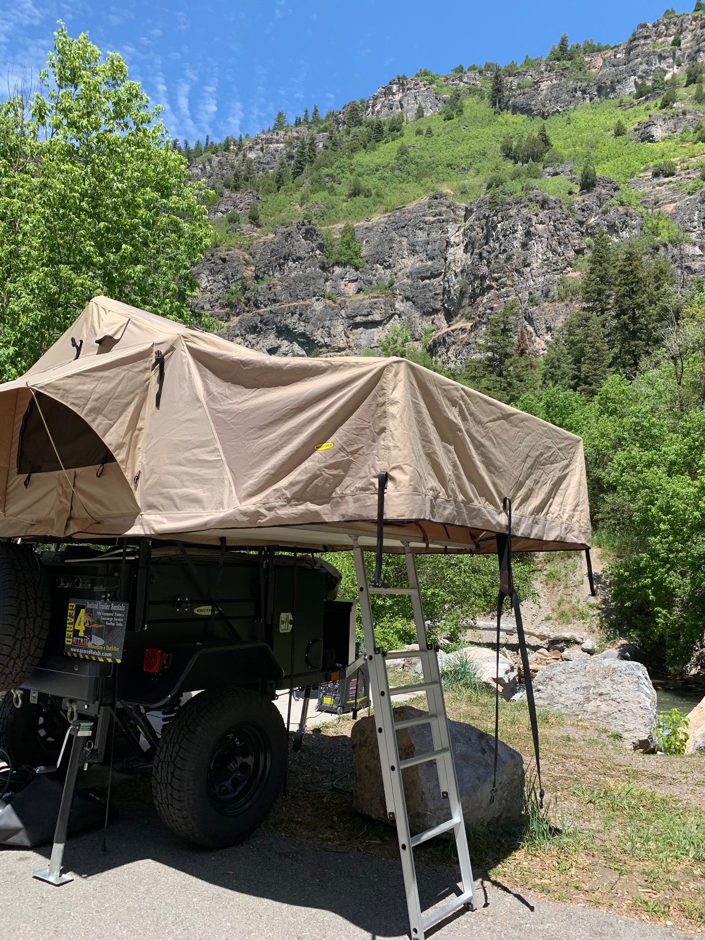 Explore nature! An overland trailer with a rooftop tent, available for RV rental, is set up in a scenic mountain area.