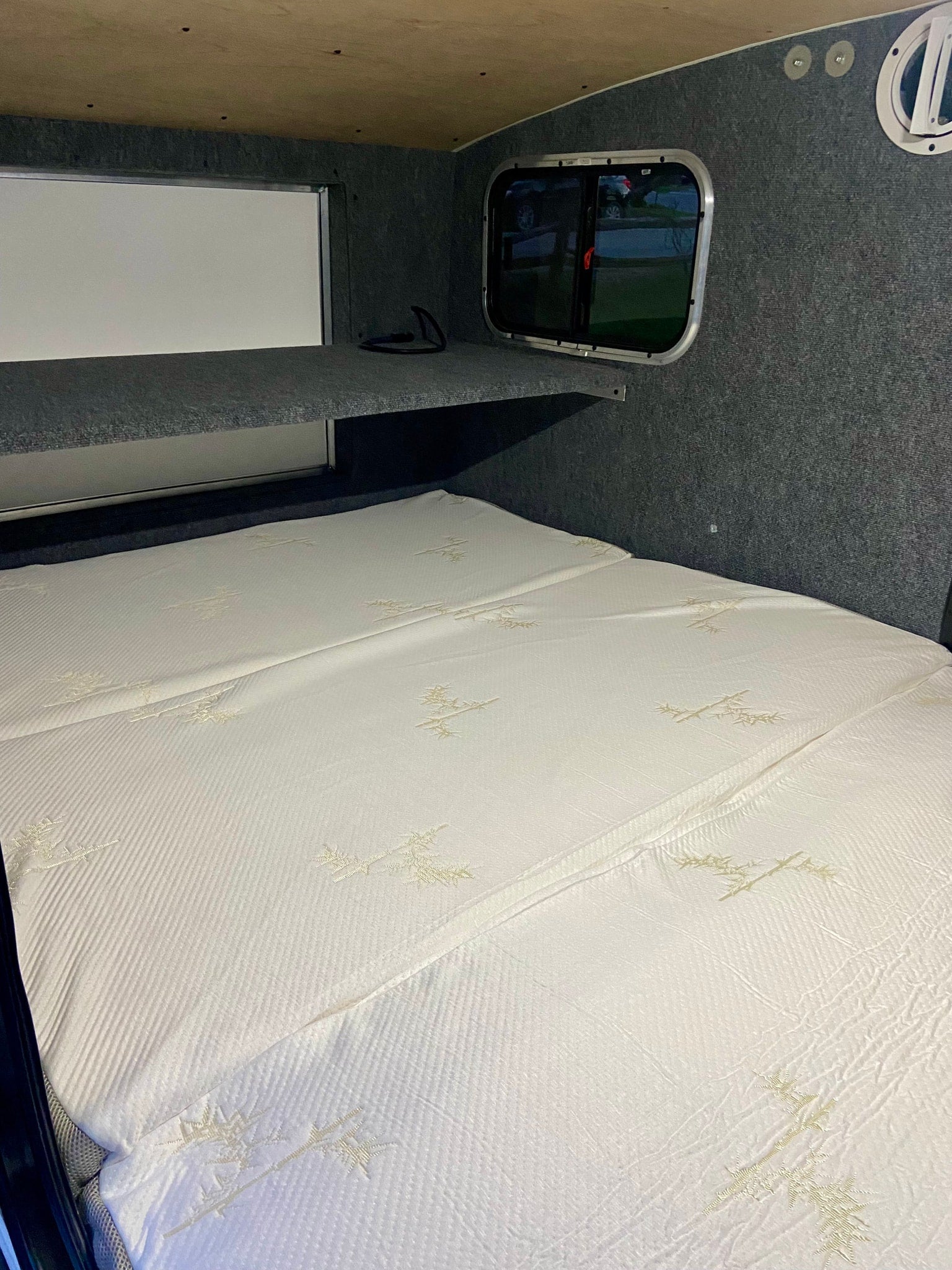 Comfortable RV rental sleeping area featuring a plush mattress, overhead shelf, and window views. Ready for adventure!