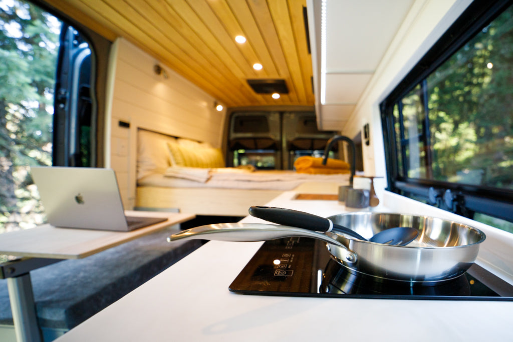 Bright RV rental interior: modern kitchen, cozy bed, laptop desk, and scenic window view. Ideal for van life.