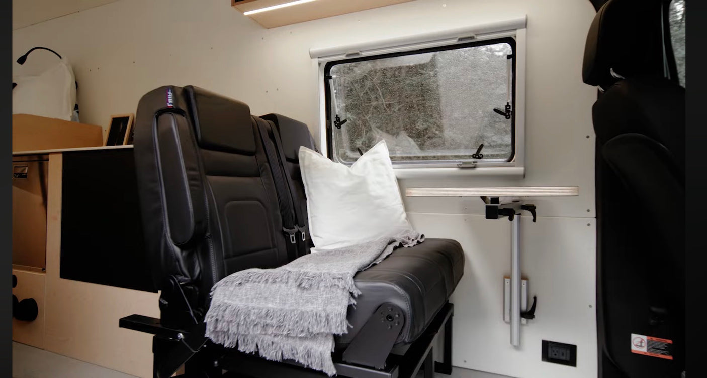 This rv rental's comfortable interior features black leather seats with a pillow and throw, a foldable table, and a window view.