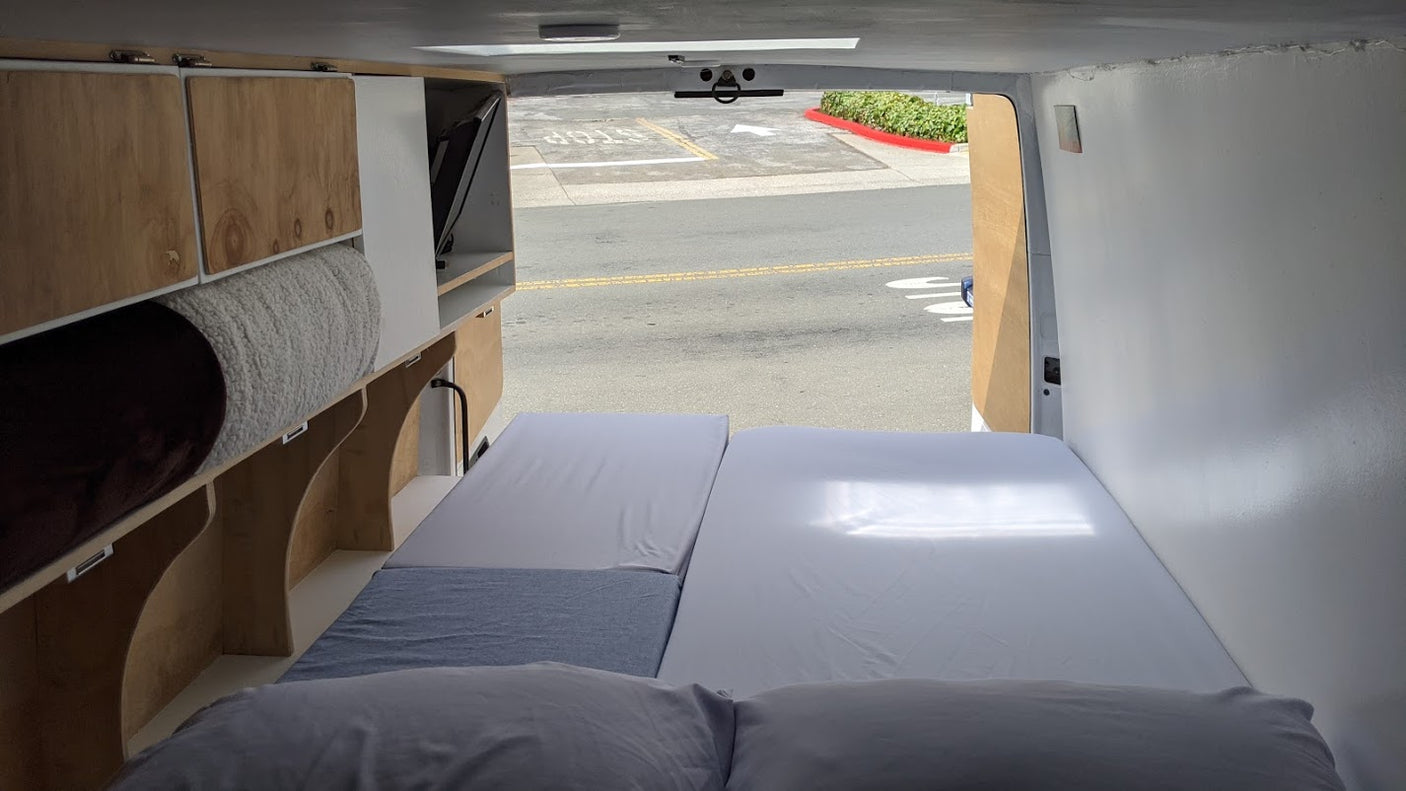 RV rental's custom wood interior: bed, cabinetry, and stored items. Street view from the open rear doors.