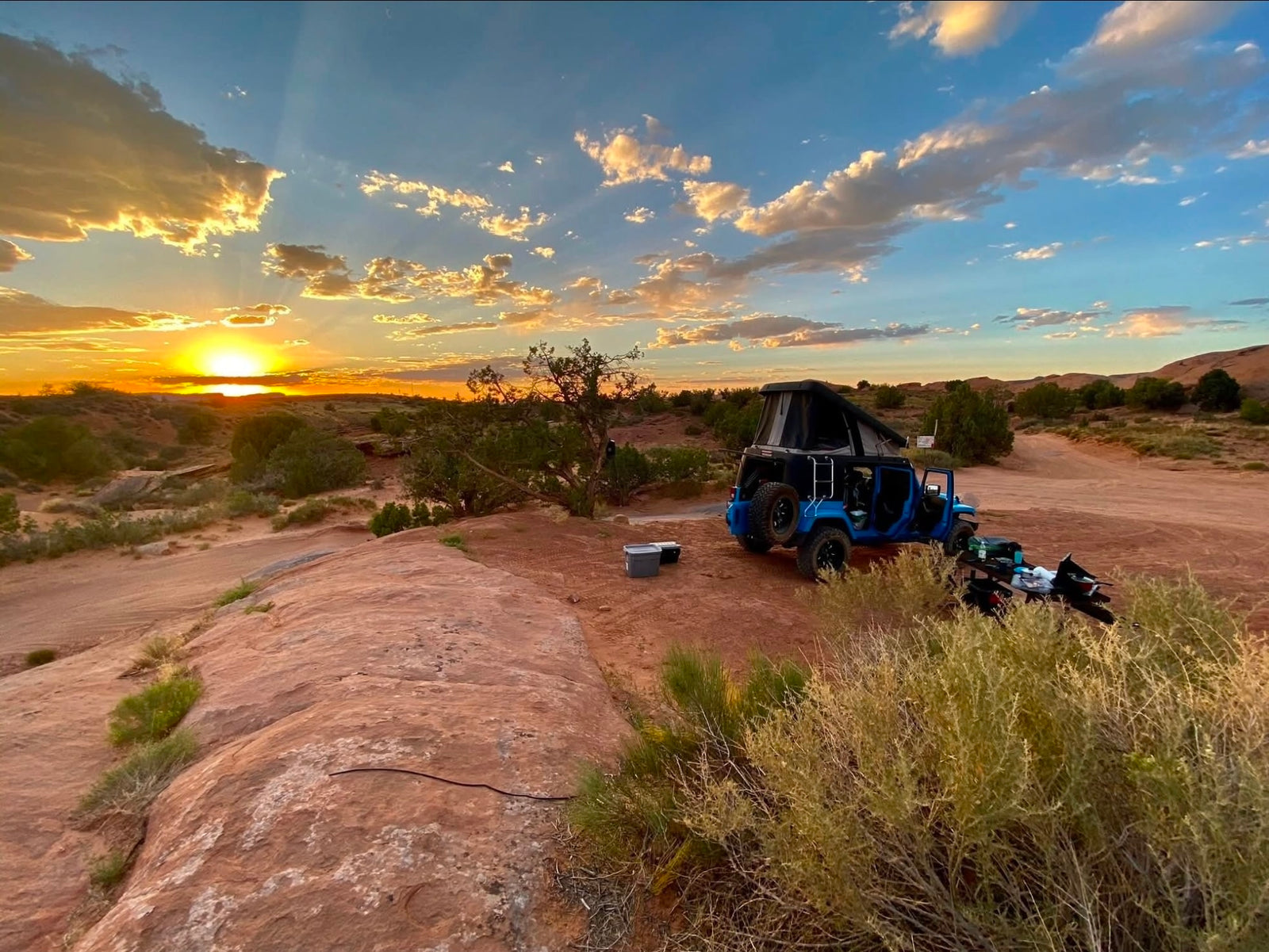 majestic red cliffs rising. Perfect for rugged adventure travel.|Adventure awaits! This blue Jeep RV rental splashes through a water crossing in a stunning red rock canyon. Perfect for off-road exploration.|Blue Jeep overlander RV rental with pop-up tent at a scenic desert overlook
