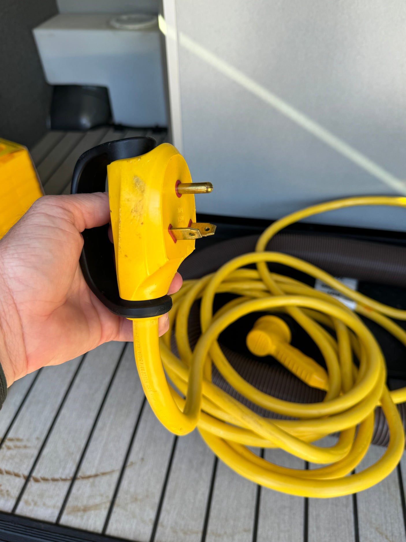 Essential for your RV rental! A hand holds a yellow 30A RV power cord plug, ready for shore power connection.