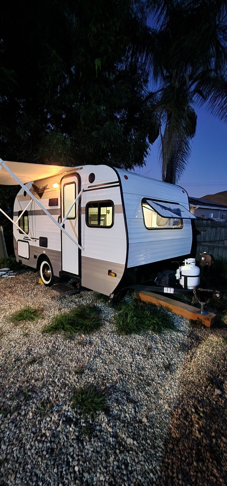 Night view of a modern RV rental, illuminated by its awning and interior lights, parked on a gravel lot. — photo 2