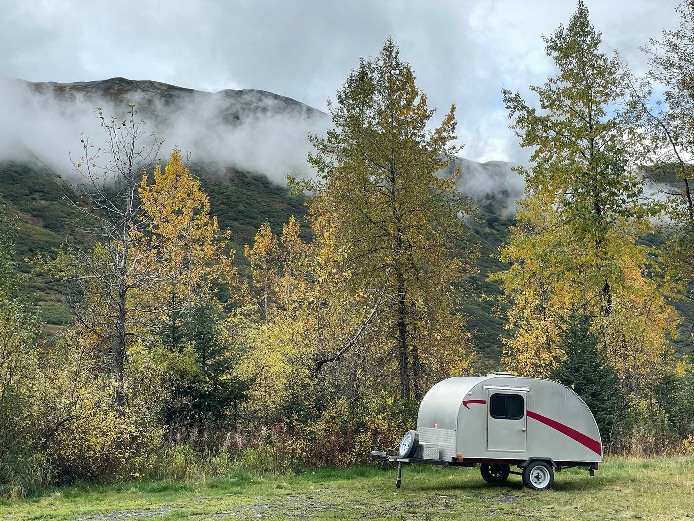 under misty mountain clouds. Scenic camping awaits!|This teardrop RV rental is parked among vibrant fall foliage and misty mountains