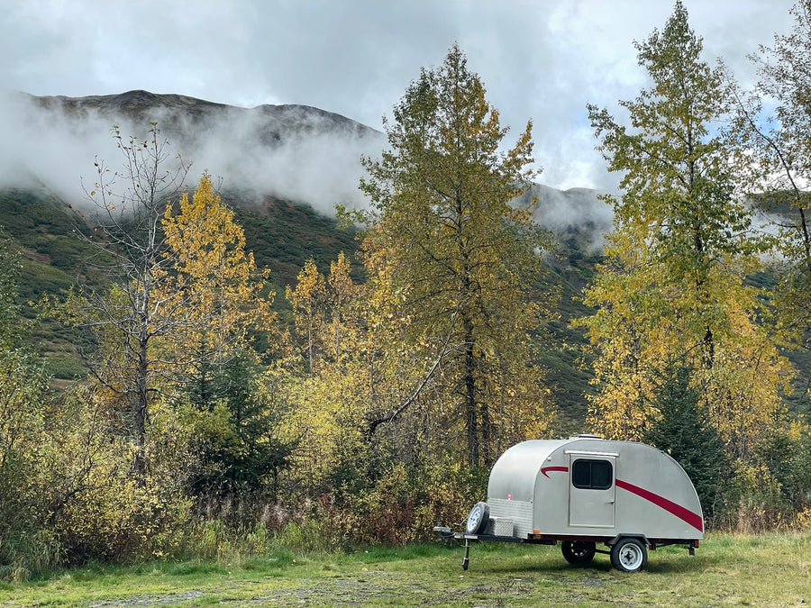 under misty mountain clouds. Scenic camping awaits!|This teardrop RV rental is parked among vibrant fall foliage and misty mountains