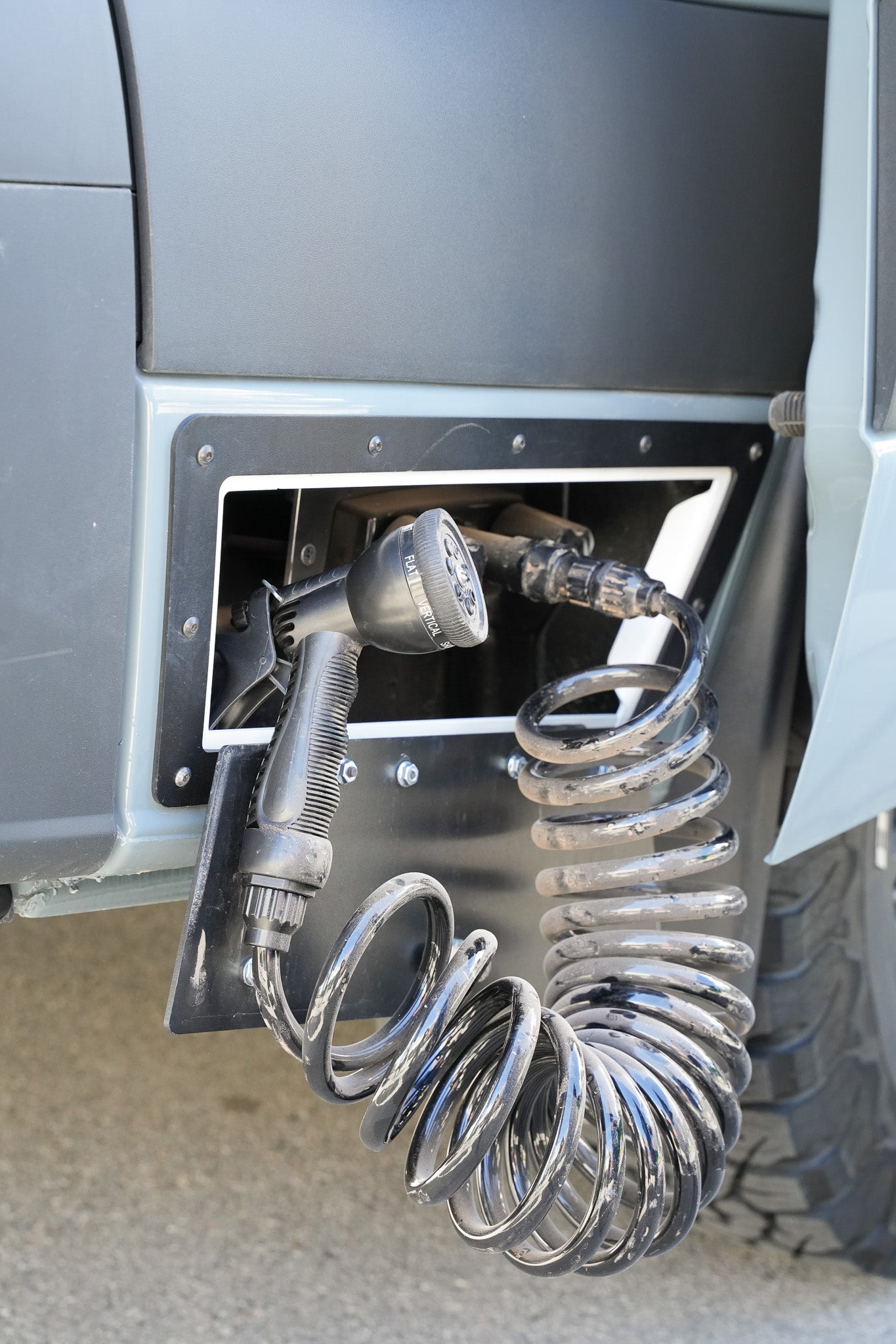 Grey RV rental's external shower featuring a black coiled hose and multi-setting spray nozzle, perfect for outdoor use.