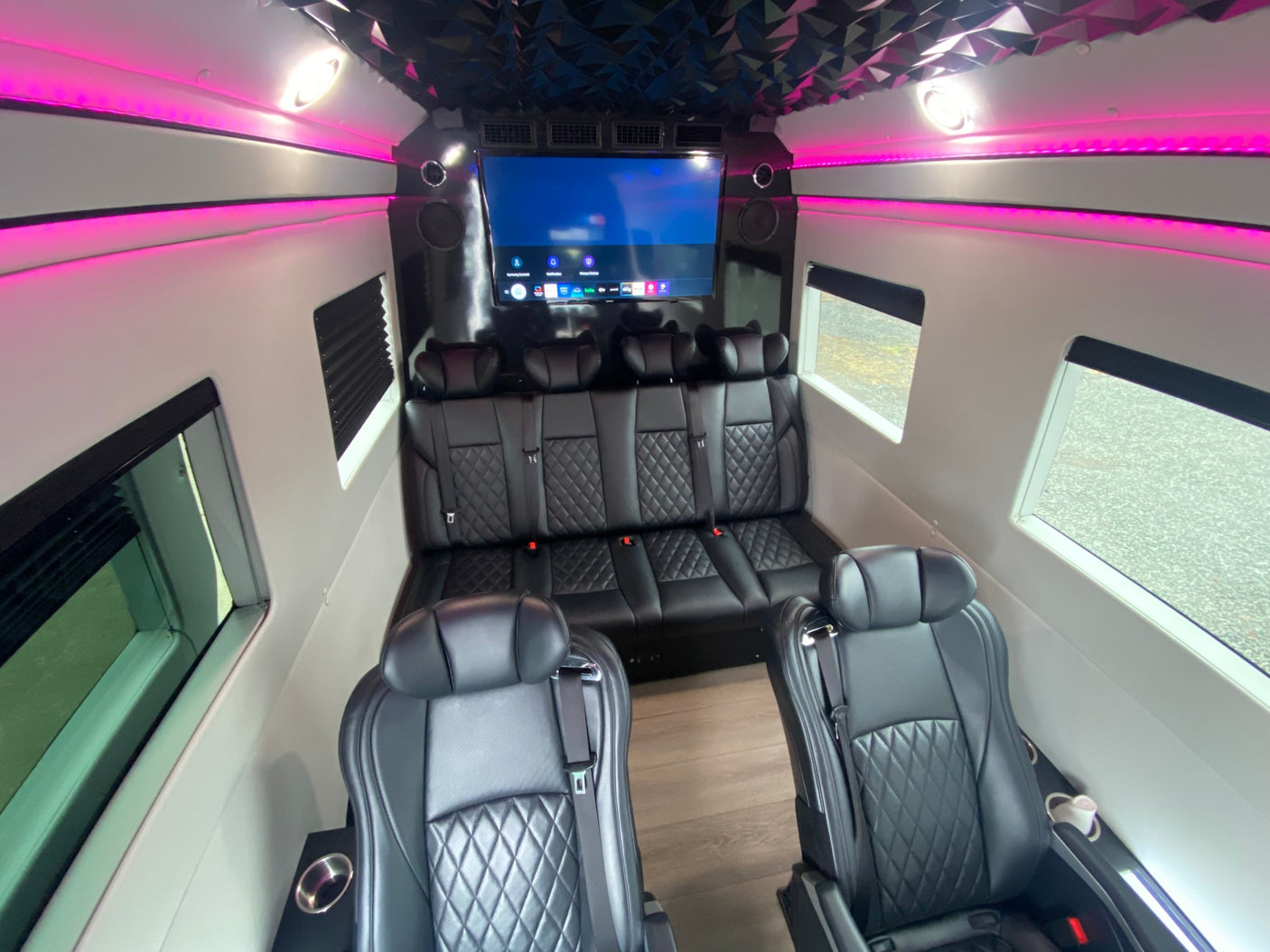 Inside a modern RV rental: black quilted leather seats, an entertainment display, and pink accent lights.