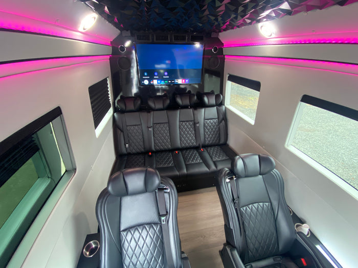 Inside a modern RV rental: black quilted leather seats, an entertainment display, and pink accent lights.