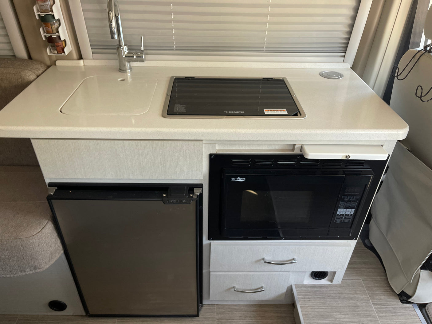 RV rental kitchen with a bright countertop, sink, Dometic cooktop, Nova Kool fridge, and High Pointe microwave, ideal for travel cooking.