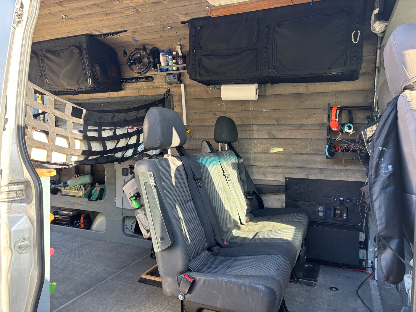 RV rental van interior with custom wood walls, multi-person seating, and overhead storage for travel essentials.