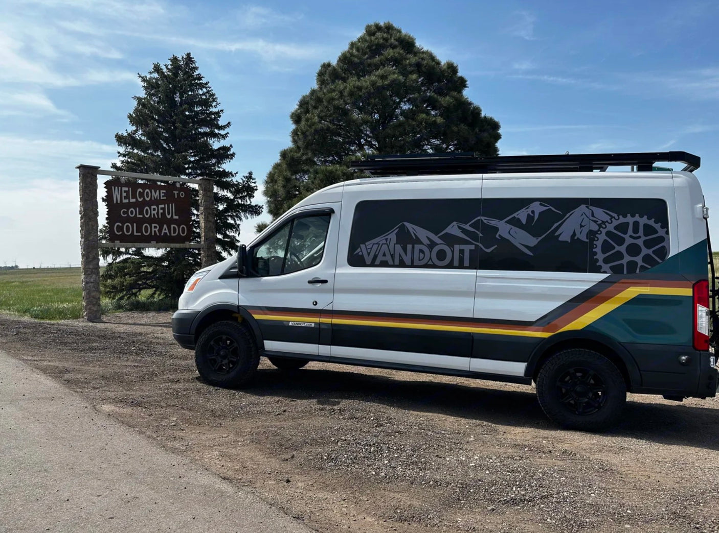 White custom Vandoit rv rental van beside the "Welcome to Colorful Colorado" sign.