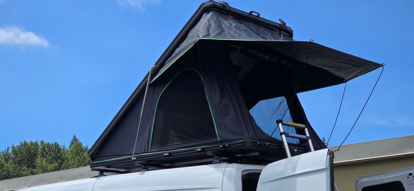 Black rooftop tent deployed on a white RV rental van, open and ready for camping under a bright blue sky.