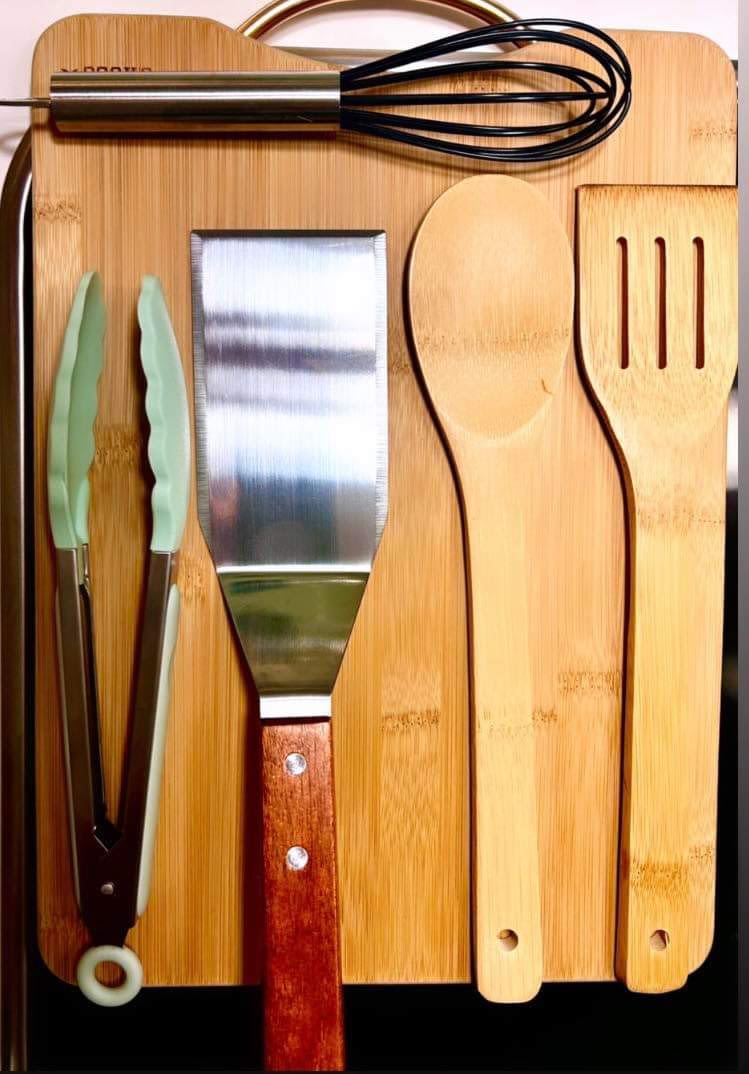 Essential kitchen tools like tongs, spatulas, and whisk, neatly arranged on a bamboo board, perfect for your next RV rental adventure.
