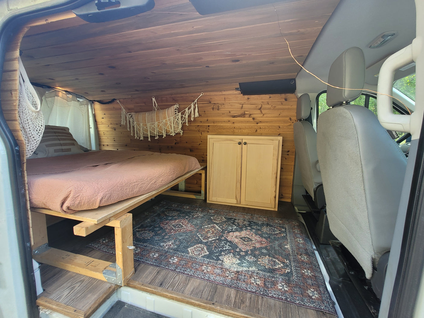 Step into this cozy RV rental's wood-paneled interior. Features a comfy bed, cabinet, and decorative rug for travel comfort.