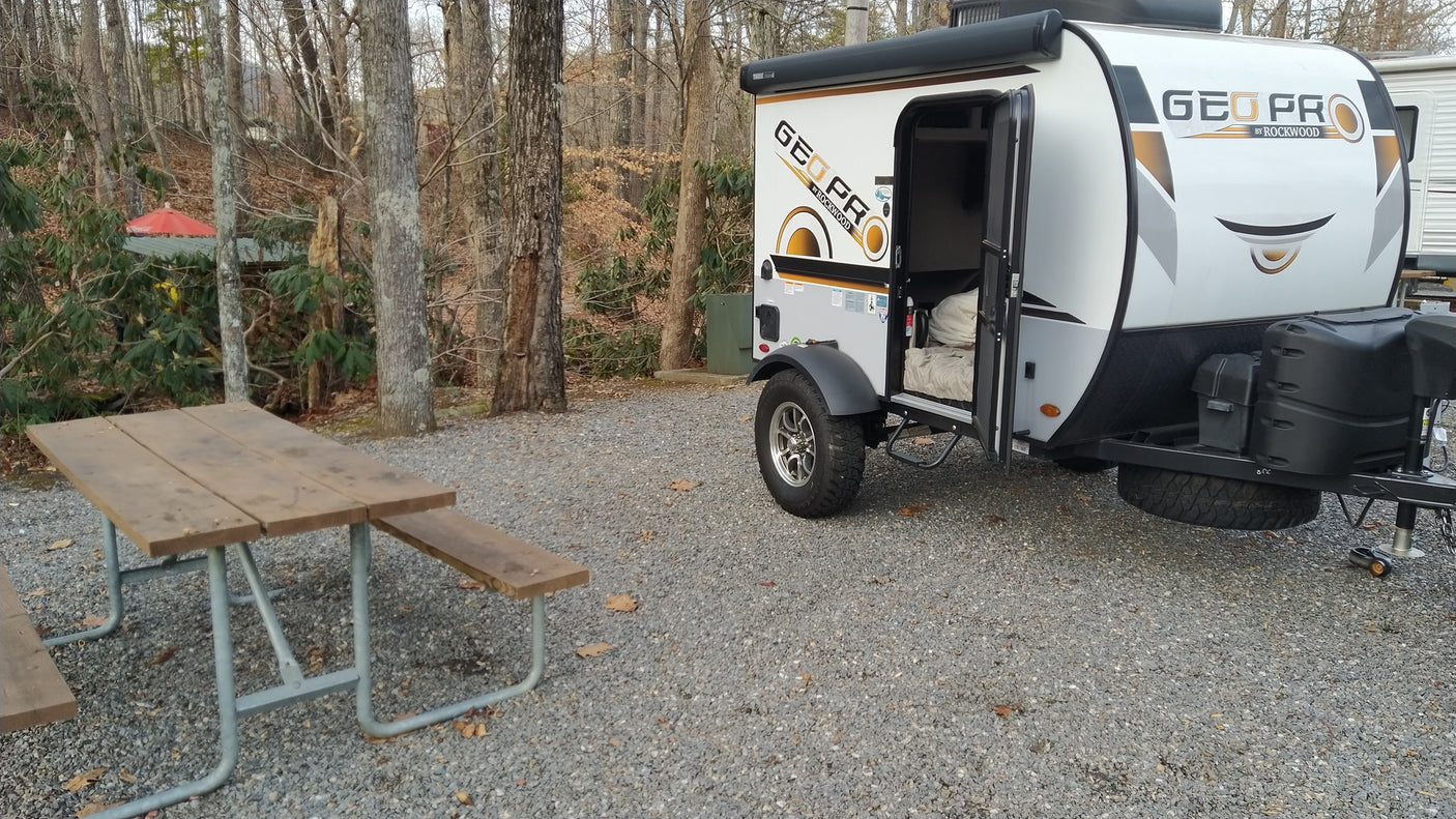 Geo Pro travel trailer RV rental at a gravel campsite with a wooden picnic table, ready for outdoor adventures.