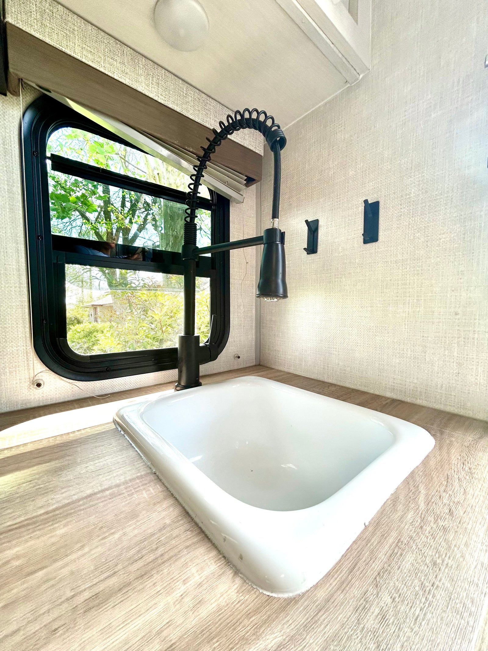 RV rental kitchen: a white sink, modern black faucet, wood-grain counter, and window with outdoor tree views.