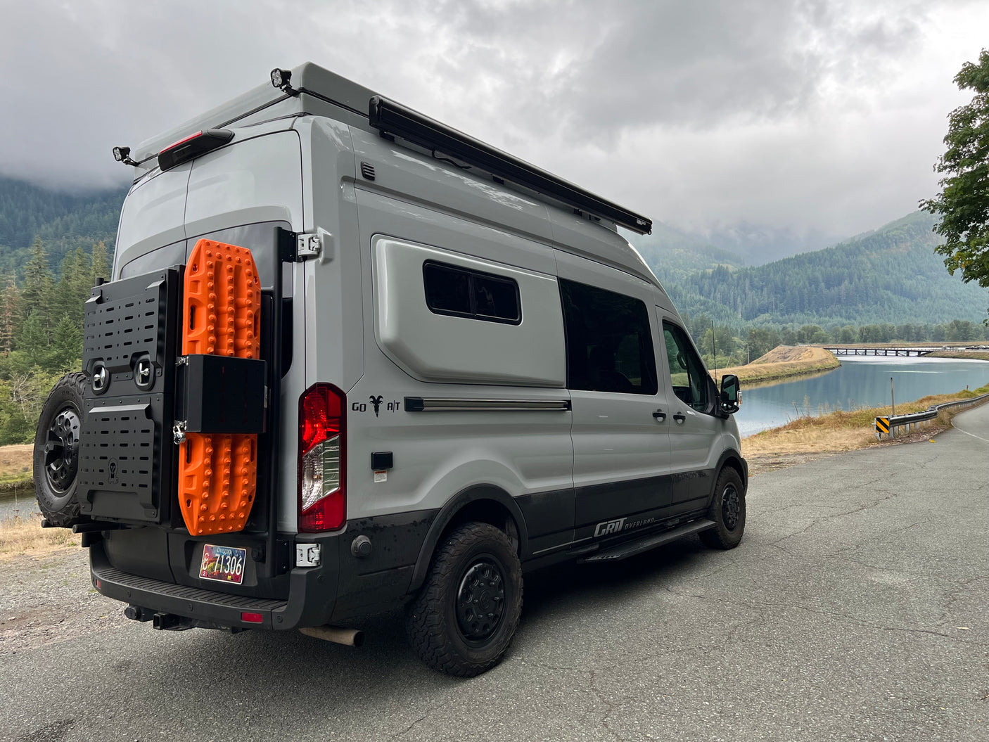 Custom grey camper van parked by a scenic river and mountains, ready for your next RV rental adventure.