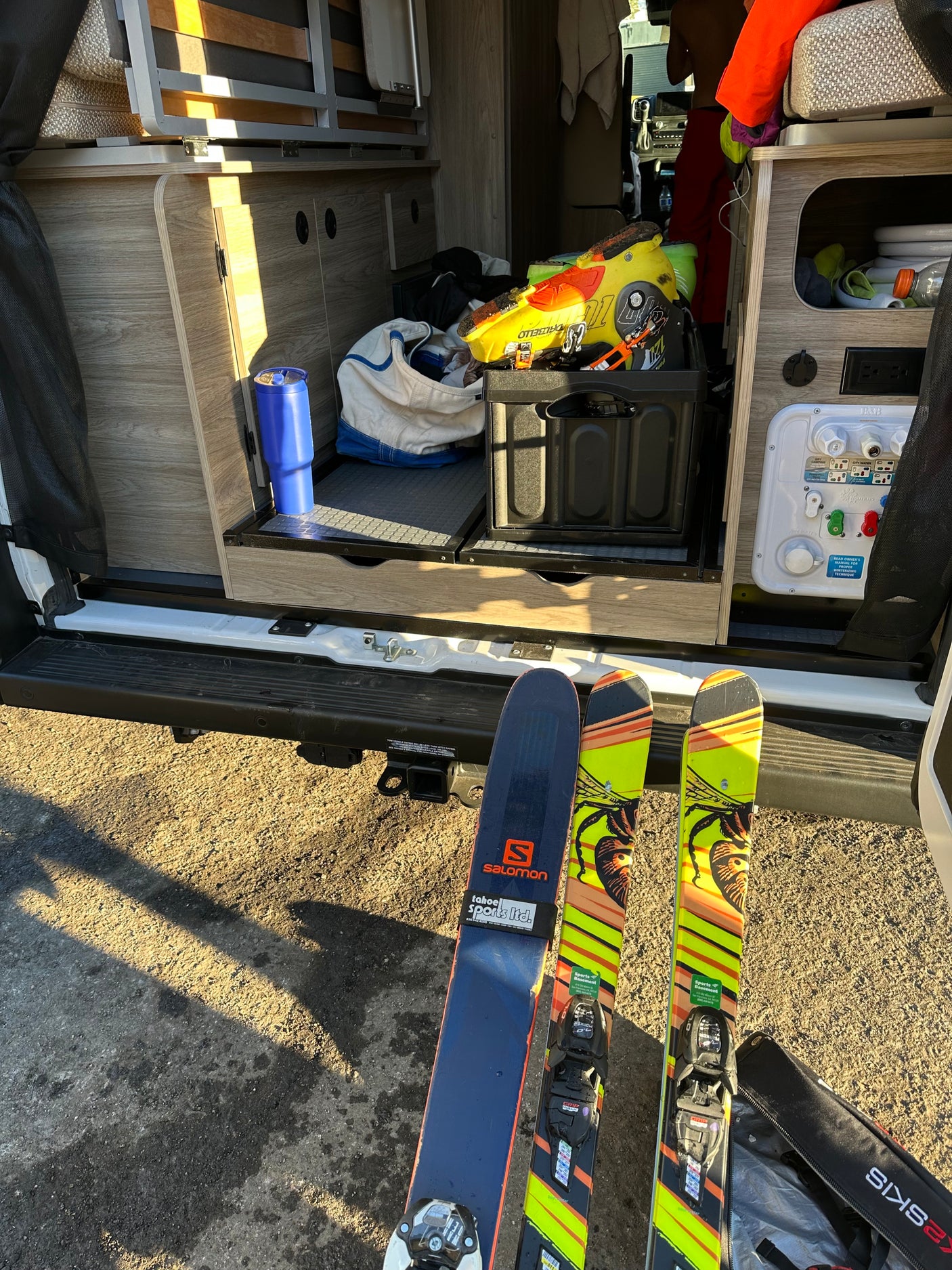 RV rental prepped for skiing. Skis & boots out; camper van interior shows storage, water hookups, and bed.