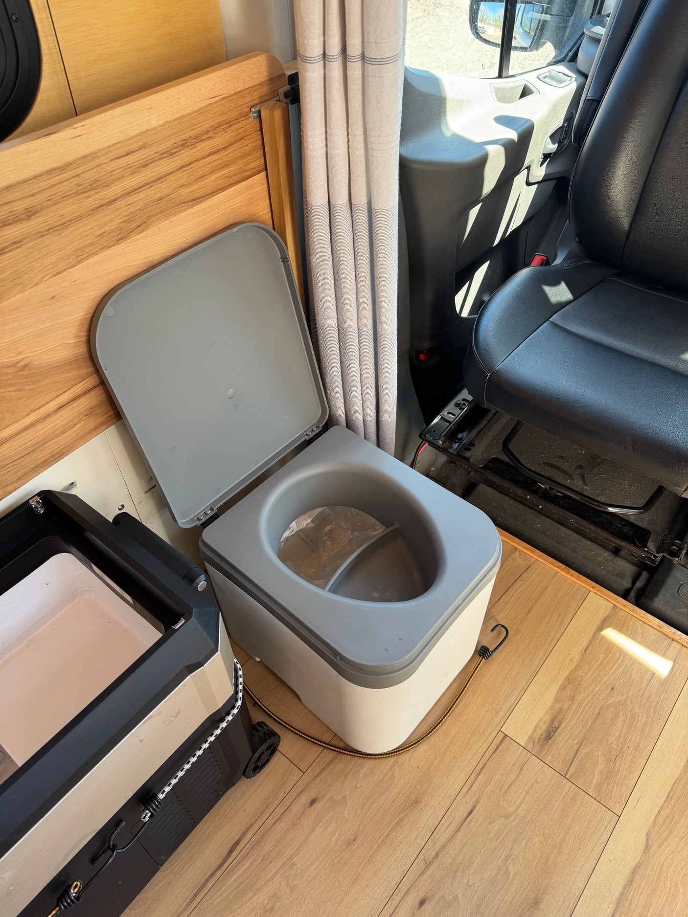 RV rental: Camper interior with a portable composting toilet, small fridge, and passenger seat.