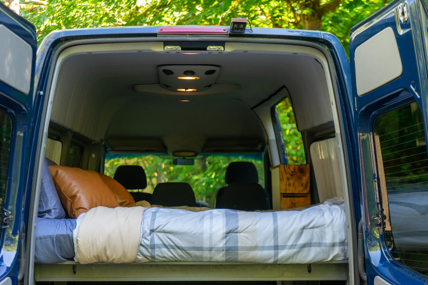 Open rear doors of a blue camper van revealing a comfy bed. Experience van life with this RV rental.