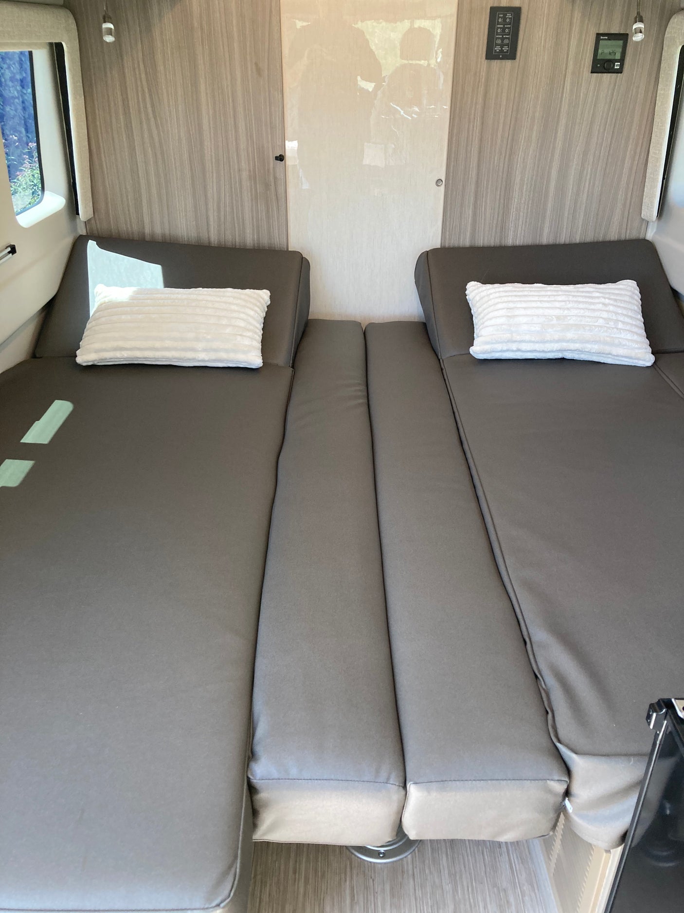 Spacious RV rental interior with two grey convertible beds, soft white pillows, and wood-paneled walls.